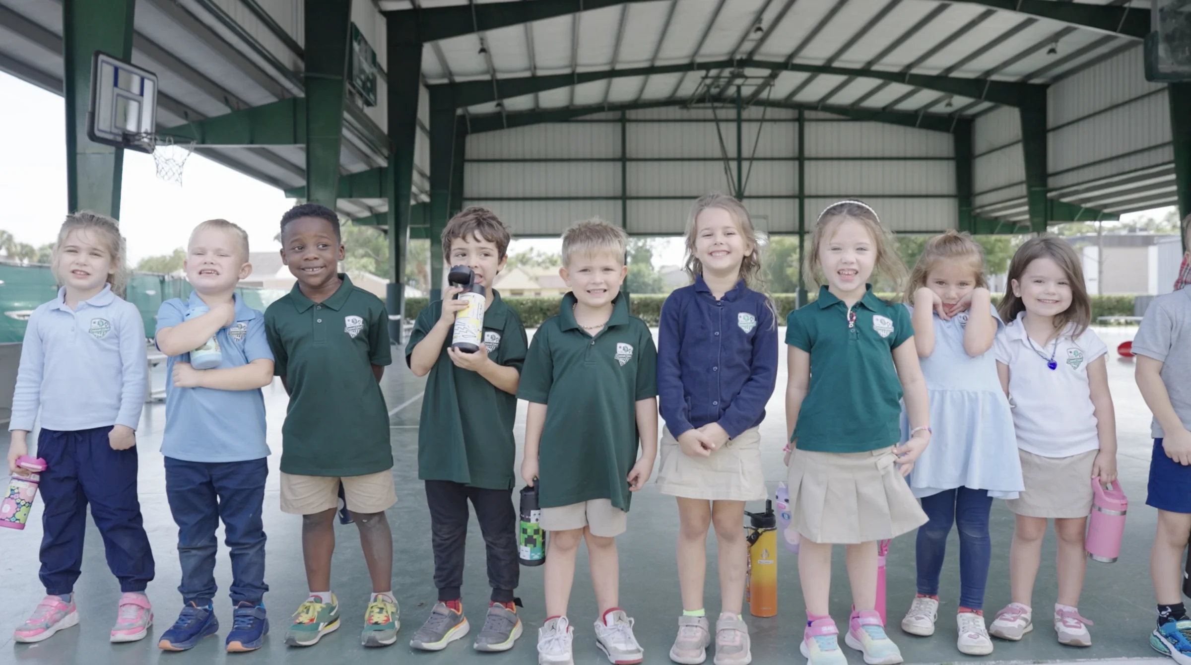 A line of young students in green uniforms under the covered court